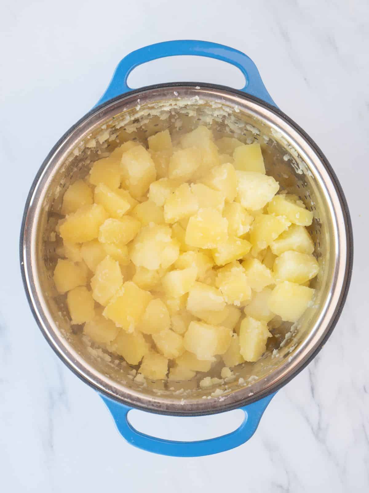A colander full of strained boiled cubed potatoes placed in a dutch oven.