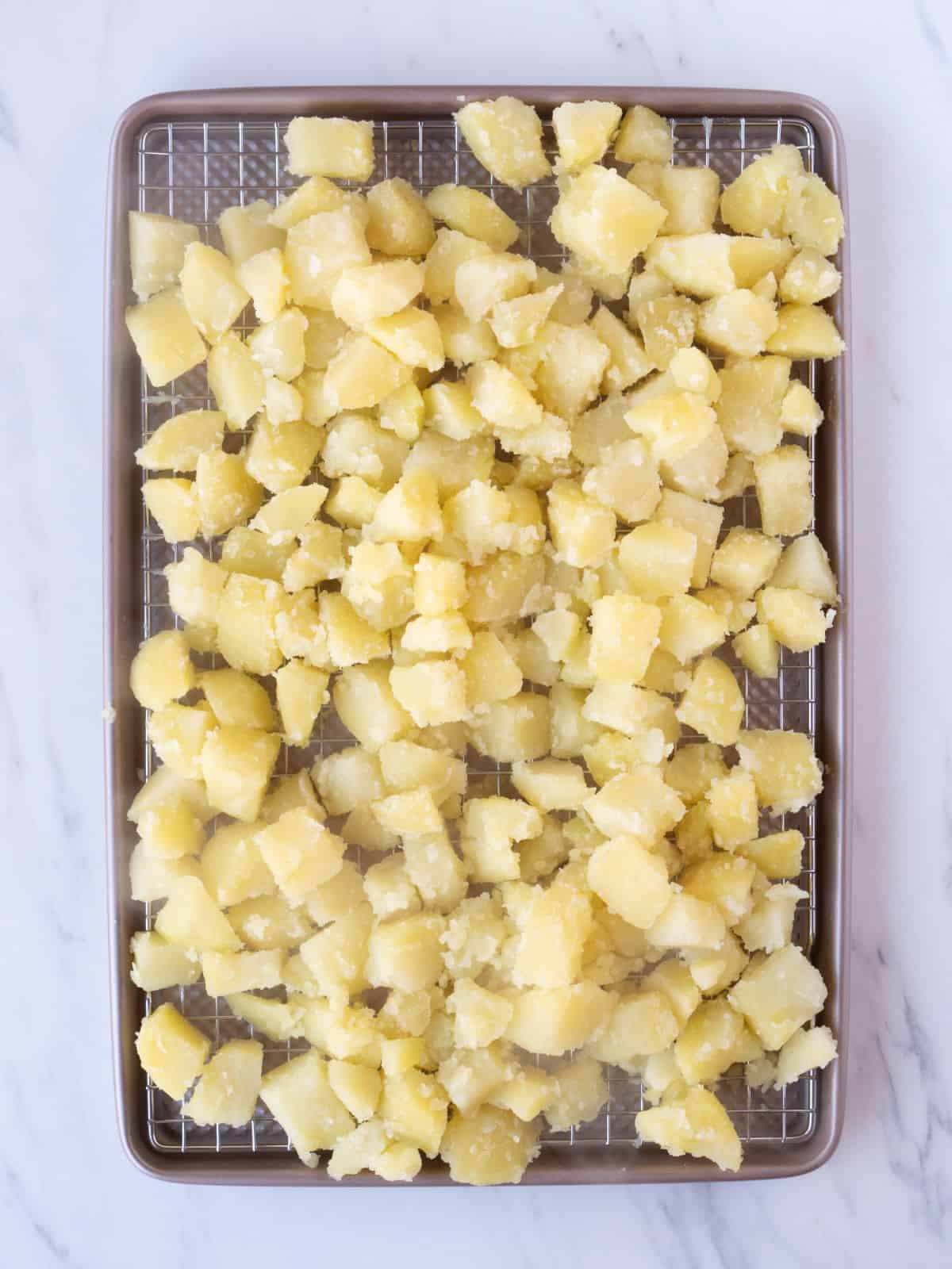 A wire rack placed on a baking sheet with cubed boiled potatoes.