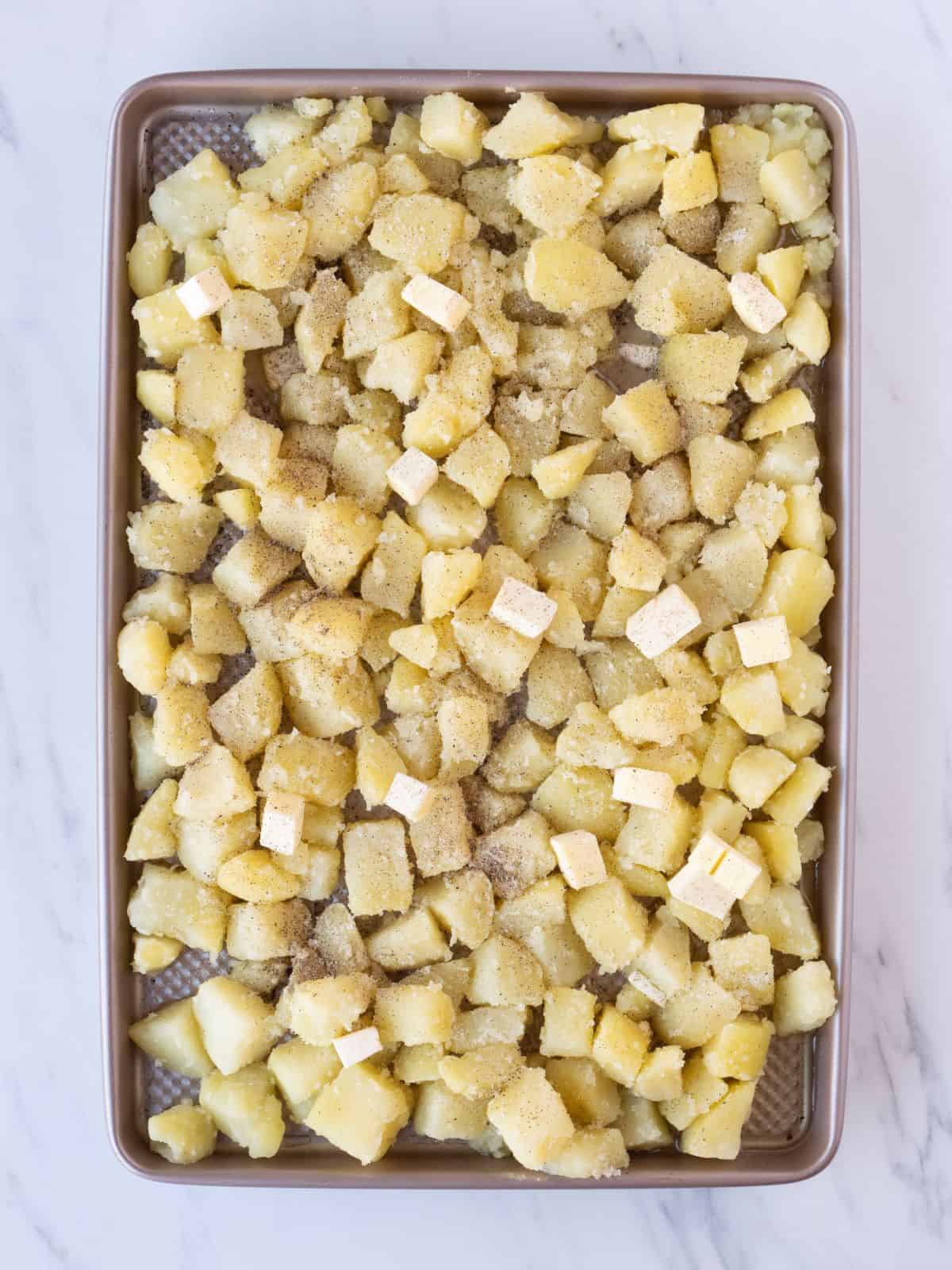A baking sheet with boiled cubed potatoes on it that are seasoned with salt and pepper.