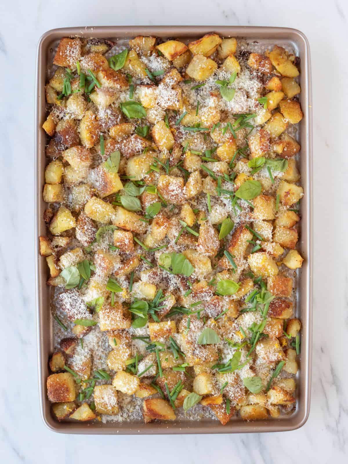 A baking sheet with roasted cubed potatoes, topped with herbs and cheese.