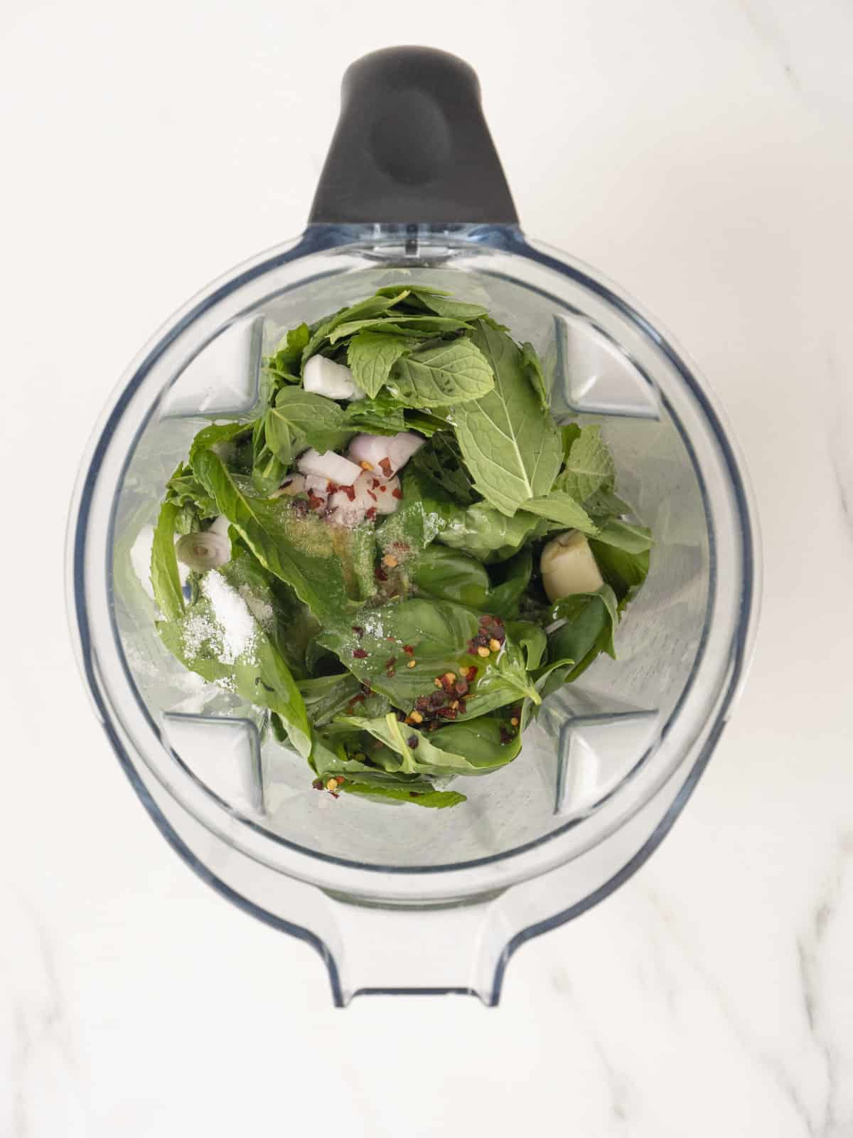 A food processor with all the ingredients to make basil mint sauce.