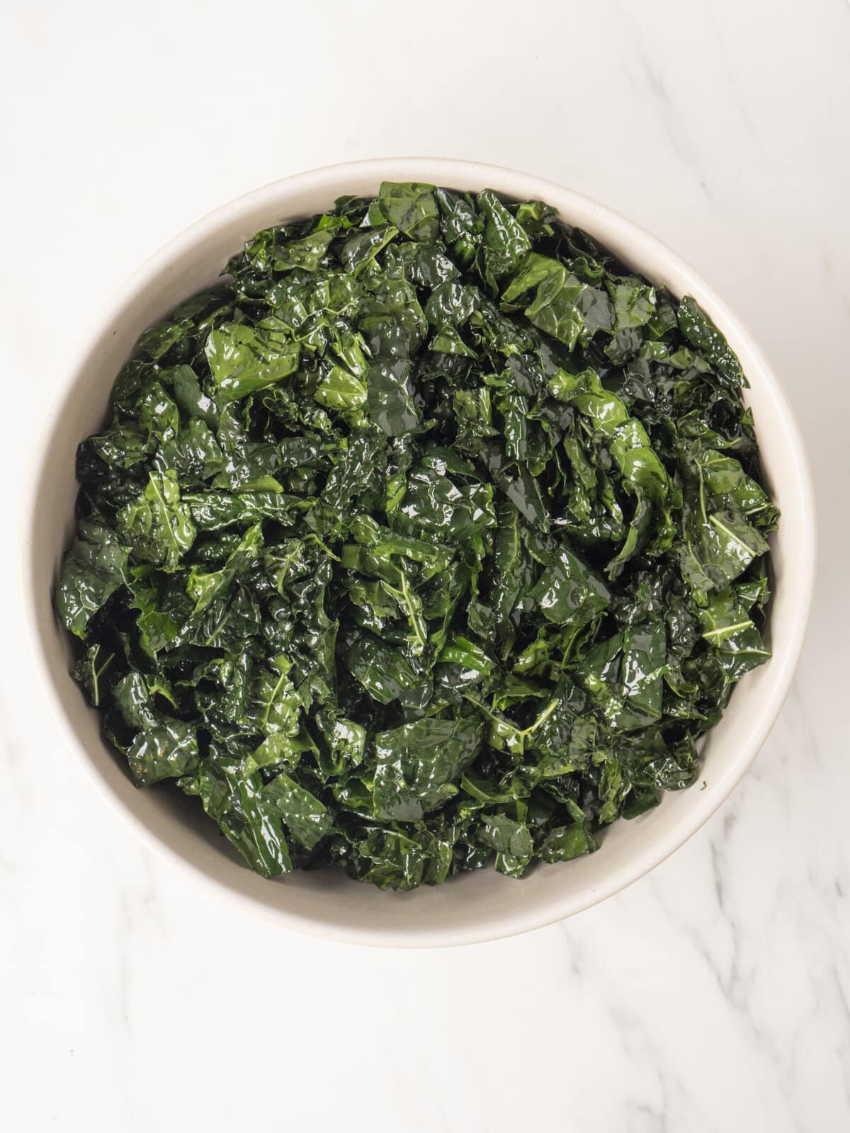 A bowl with kale drizzled with olive oil and salt and massaged with kale.