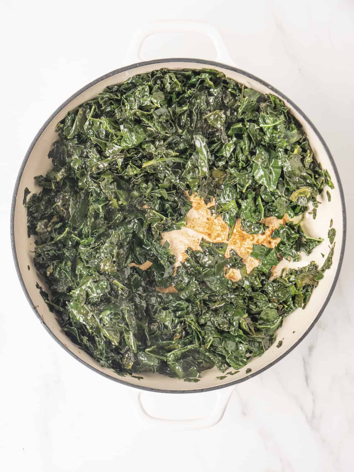 A white dutch oven with chopped kale being cooked.