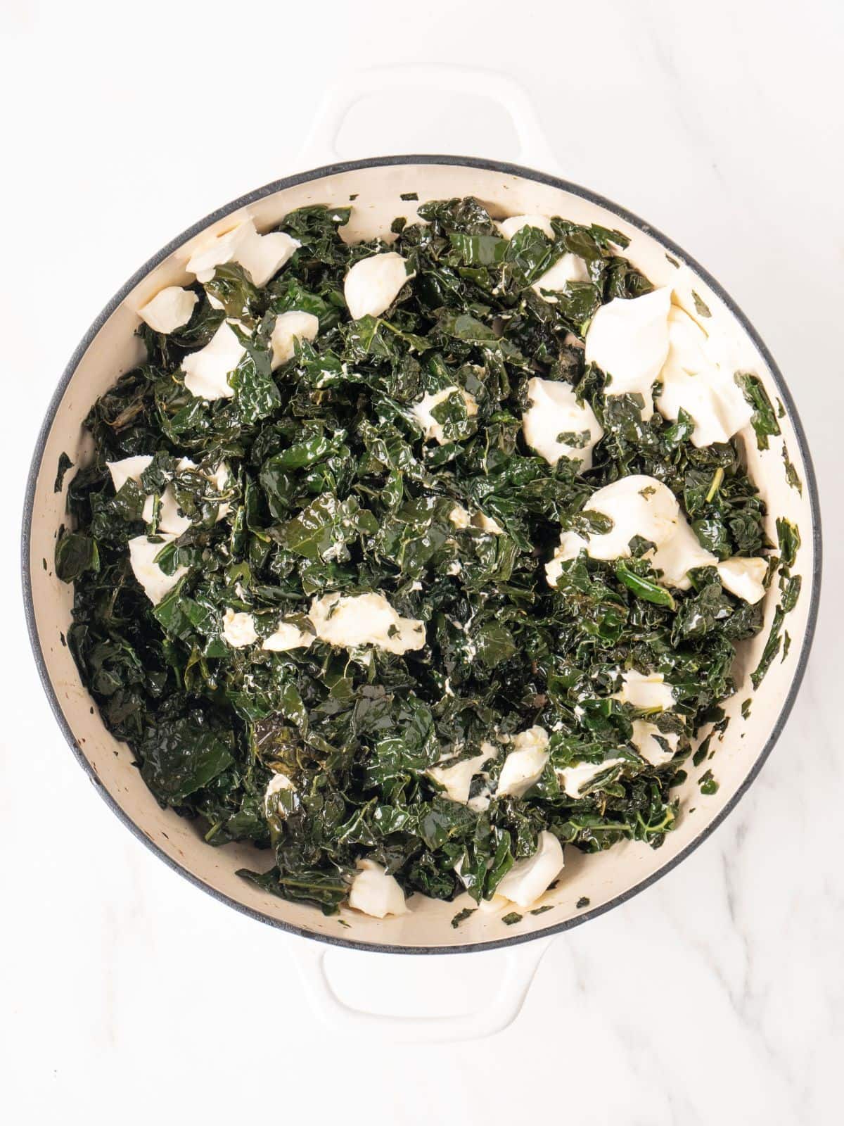 White dutch oven with kale cooked, and cream cheese topped on it.