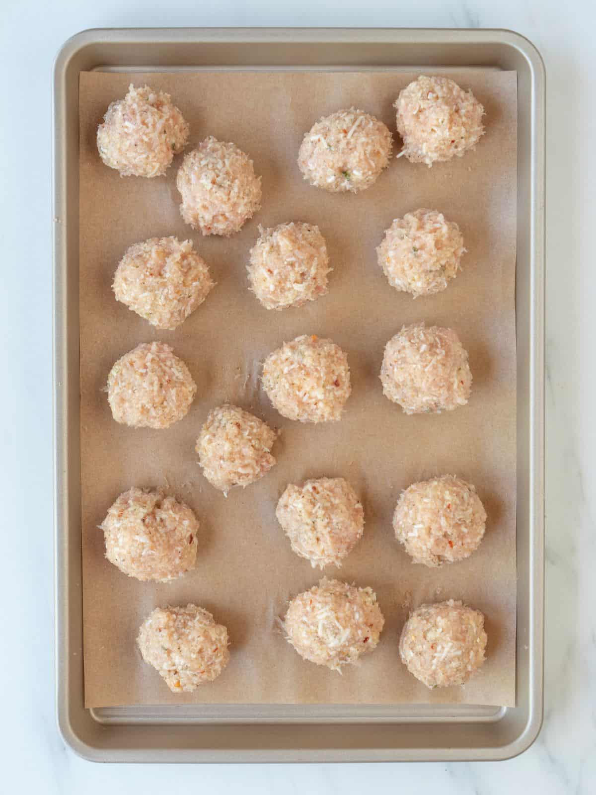 A parchment-lined baking sheet of chicken mixture shaped into meatballs.