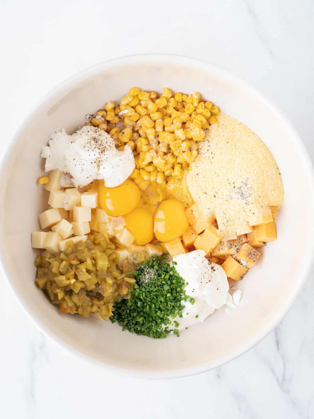 A white mixing bowl with all the ingredients to make corn soufflé.