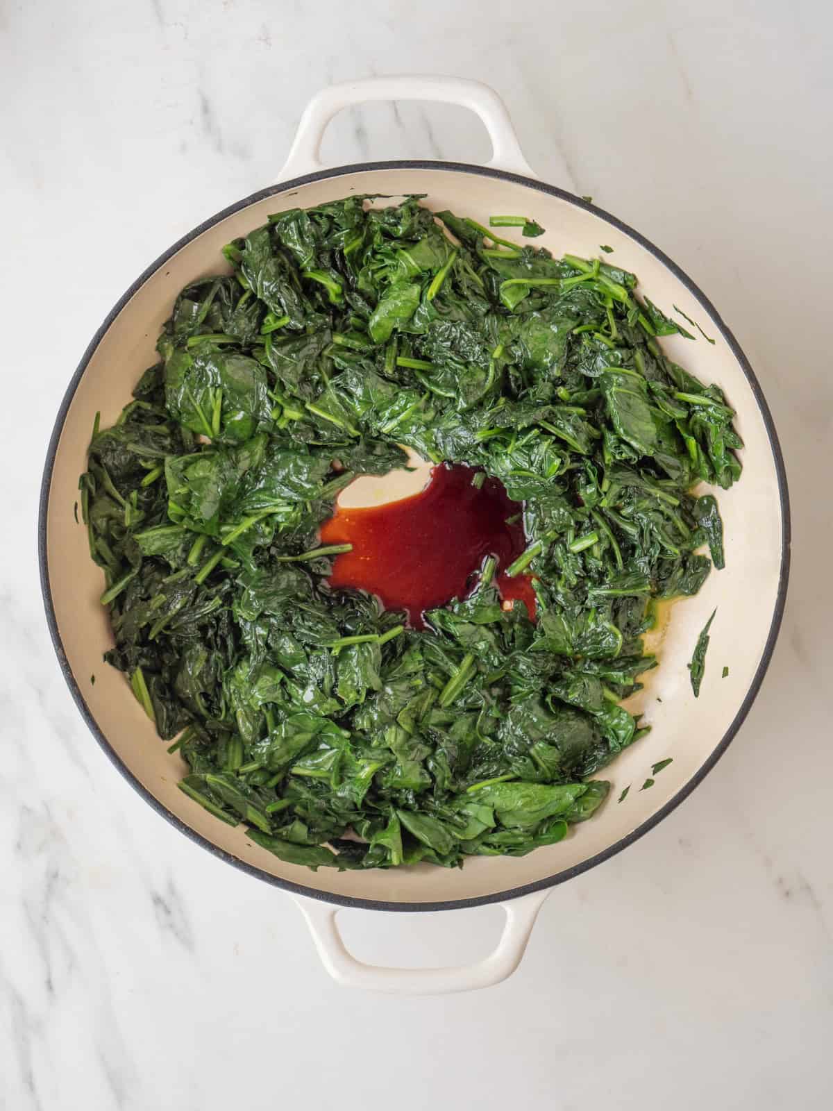 A dutch oven with spinach softened from cooking and balsamic vinegar added.