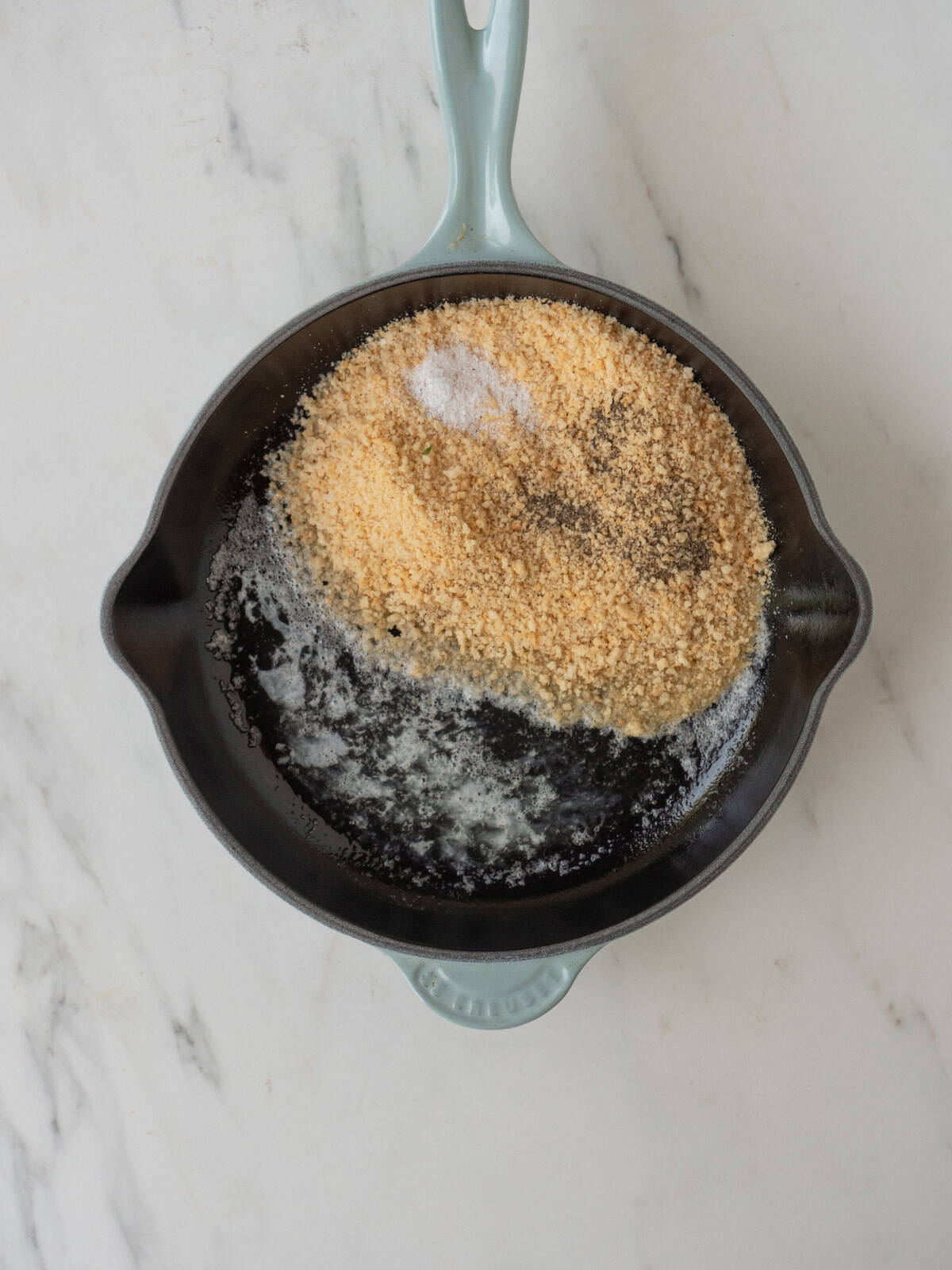 A skillet with butter melted and panko breadcrumbs added along with salt and black pepper.