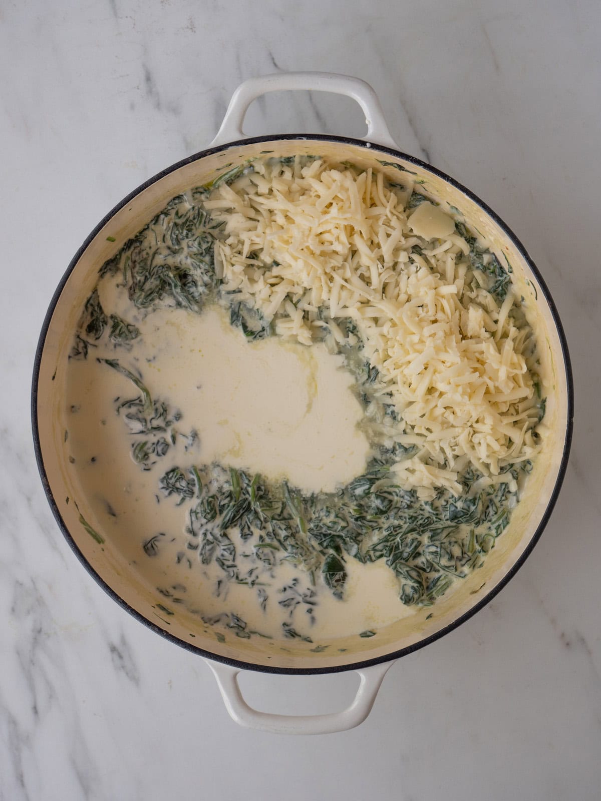 A dutch oven with cooked spinach, and shredded fontina cheese, heavy cream and lemon juice added.