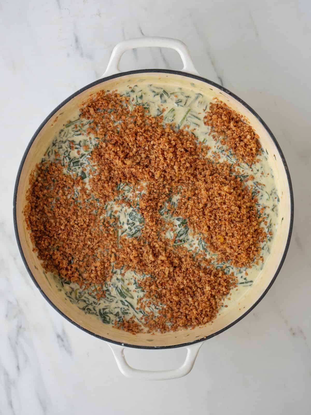 A dutch oven with creamed spinach and toasted breadcrumbs sprinkled on top.