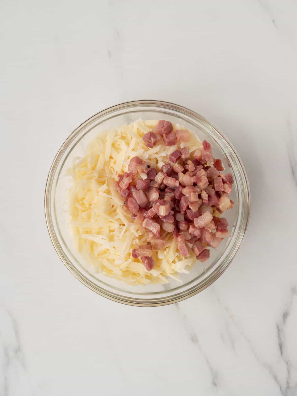 A small glass mixing bowl of cooked pancetta and shredded cheese.