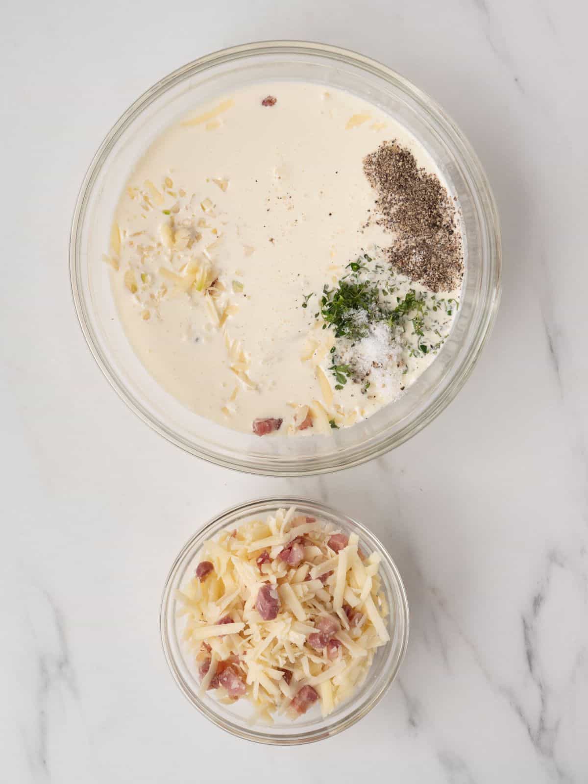 A small glass mixing bowl of cooked pancetta and shredded cheese along with a bigger glass mixing bowl of the same mixture with cream, garlic and thyme.