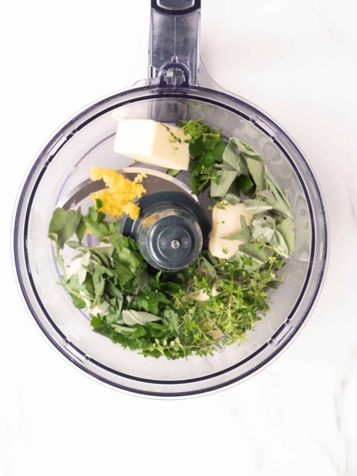 A food processor with butter and a mix of herbs to make compound butter.