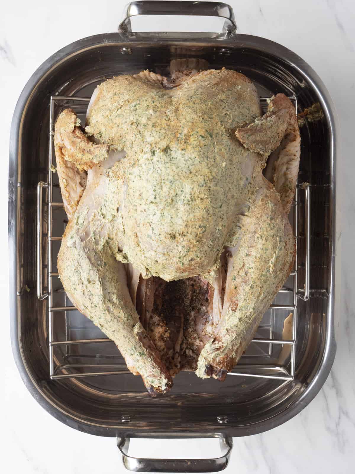 A roasting pan with a wire rack and a whole turkey placed on top, yet to be cooked.