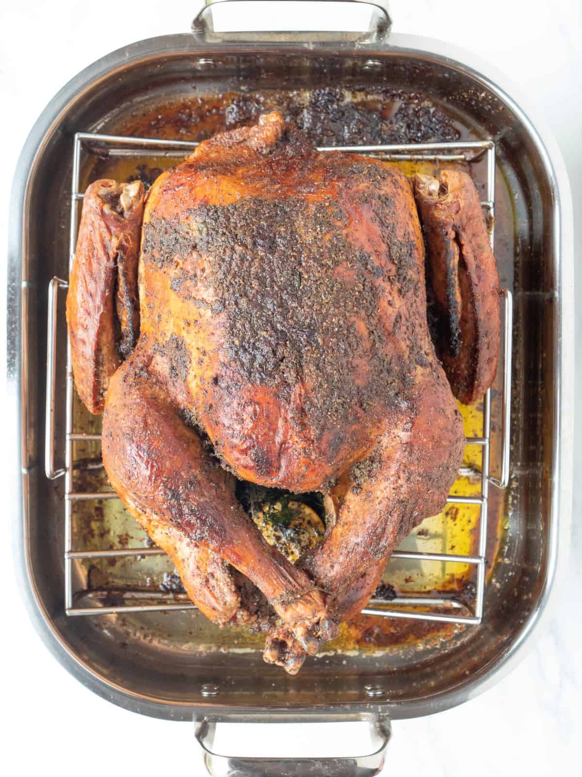 A roasting pan with a wire rack and a whole turkey placed on top, just taken out of the oven after roasting.