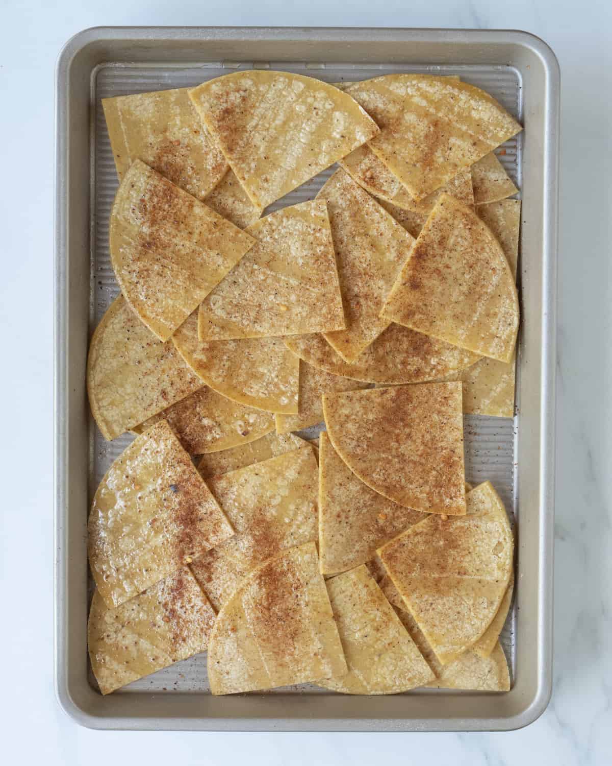 A sheet pan with corn tortillas spread out and cut into quarters seasoned with Dalkin&Co taco seasoning.