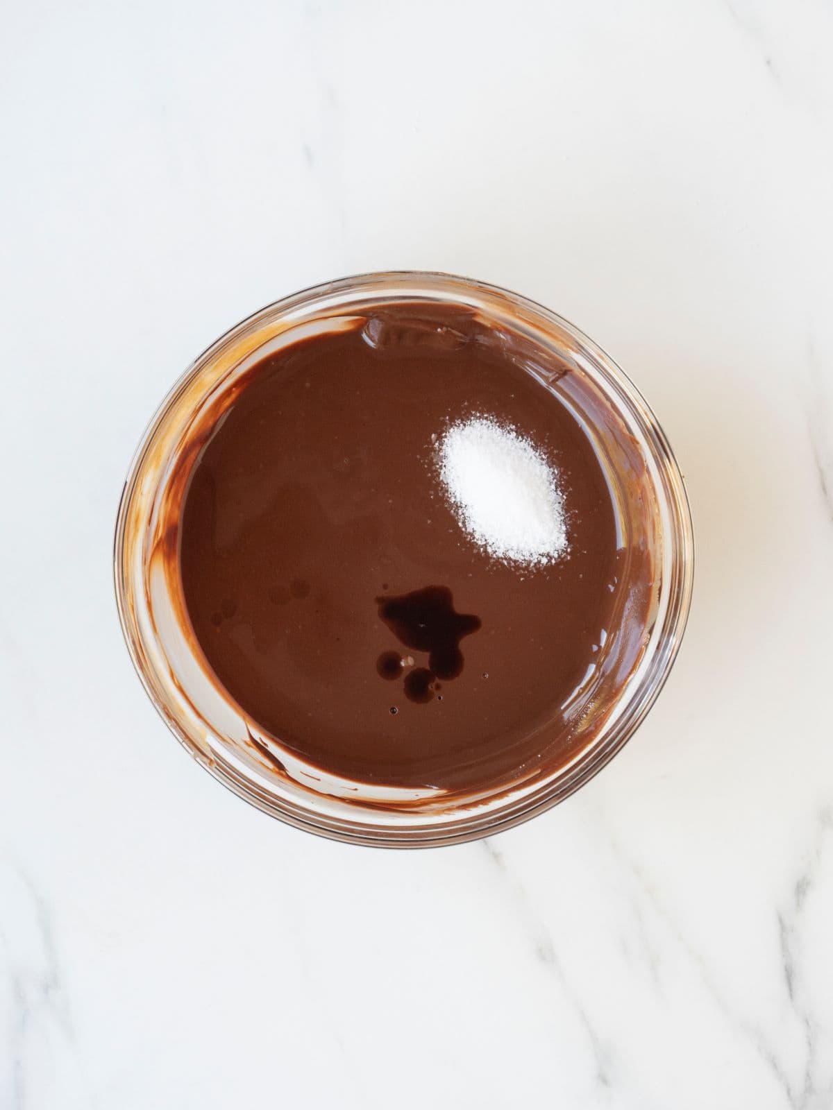 A small mixing bowl with a mix of melted chocolate, almond butter, butter, with salt and vanilla extract and chocolate extract added on top.