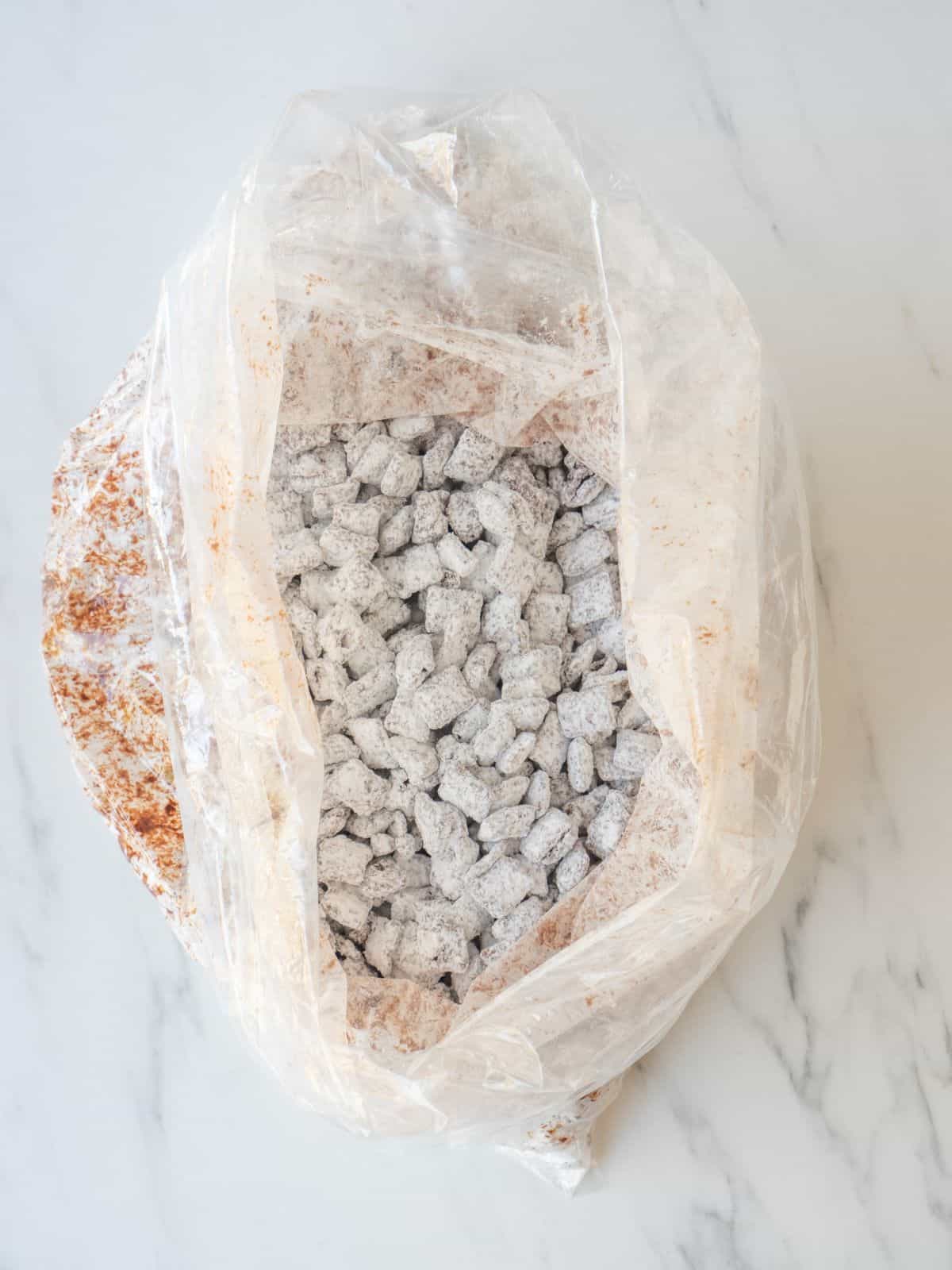 A big zip top bag with the chocolate coated Chex shaken with powdered sugar, all coated in sugar.