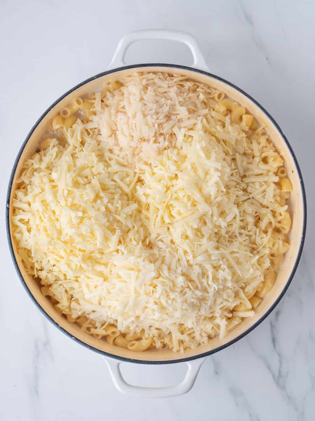 A white dutch oven with macaroni pasta in bechamel sauce topped with lots of shredded cheeses.
