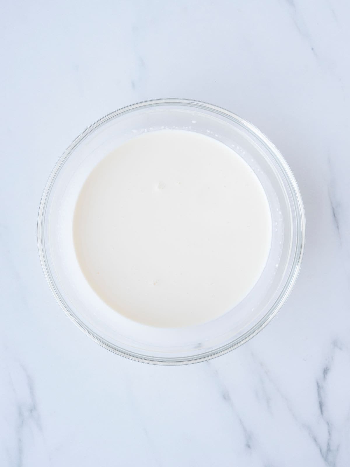 A small glass mixing bowl with a mix of milk and cream.