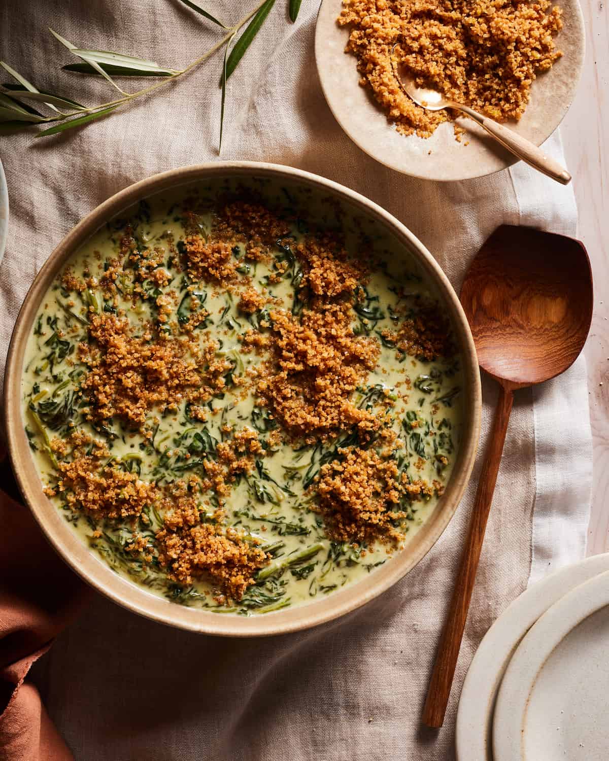 Creamed Spinach with Toasted Breadcrumbs in a large serving bowl next to a small serving bowl of breadcrumbs.  