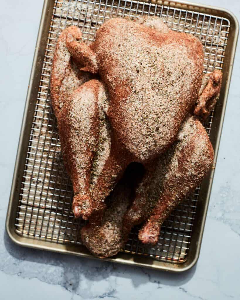 A baking sheet with a wire rack and a turkey completely covered with dry spices.