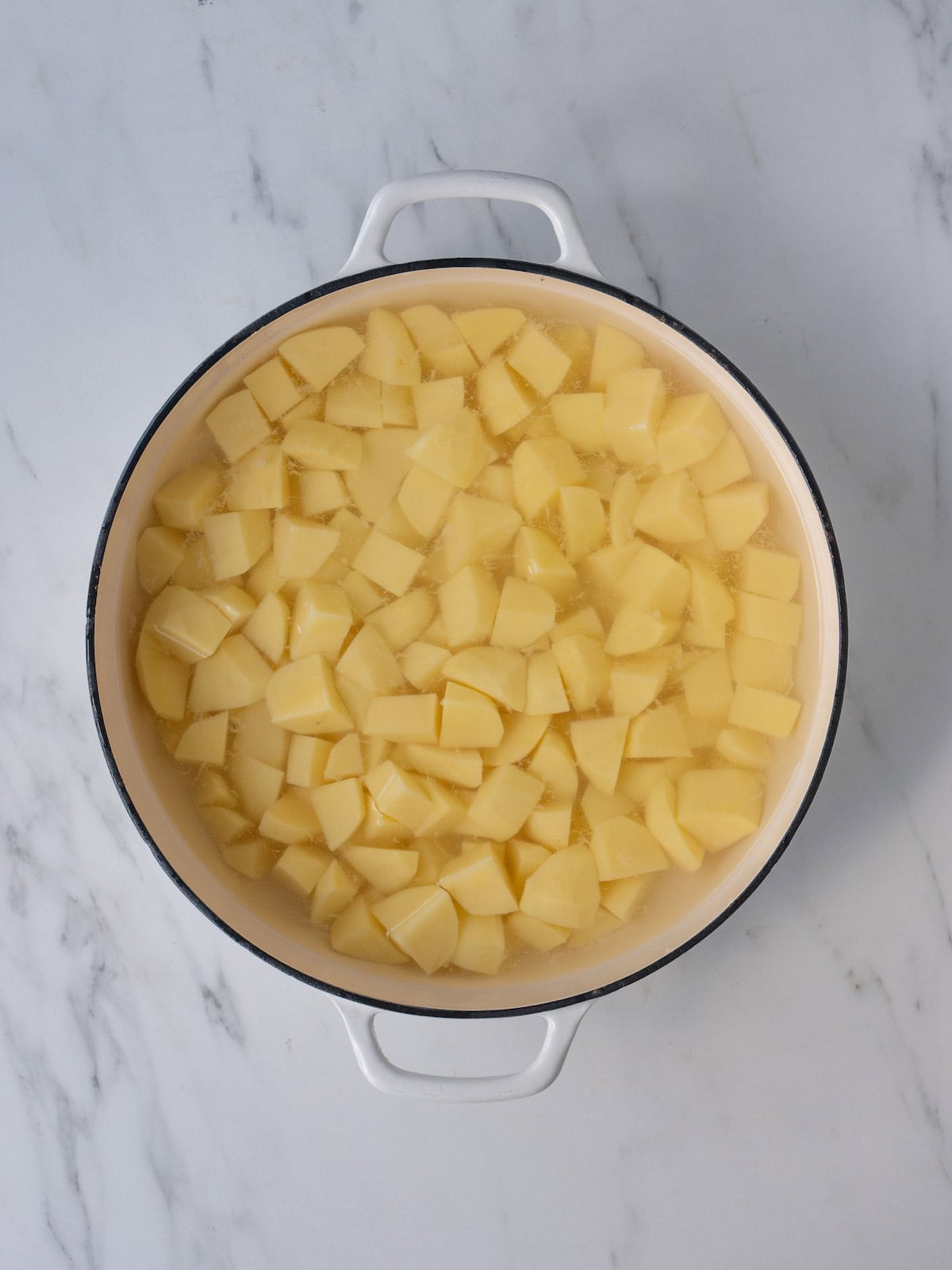 A dutch oven with cubed potatoes being boiled in water.