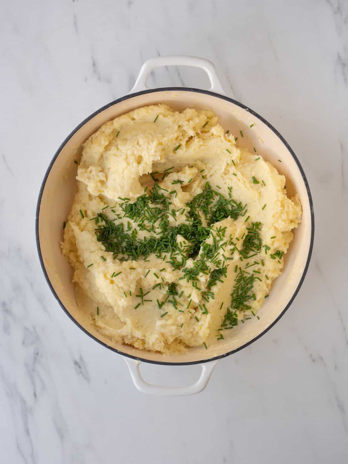 A dutch oven with white cheddar mashed potatoes garnished with chopped chives.