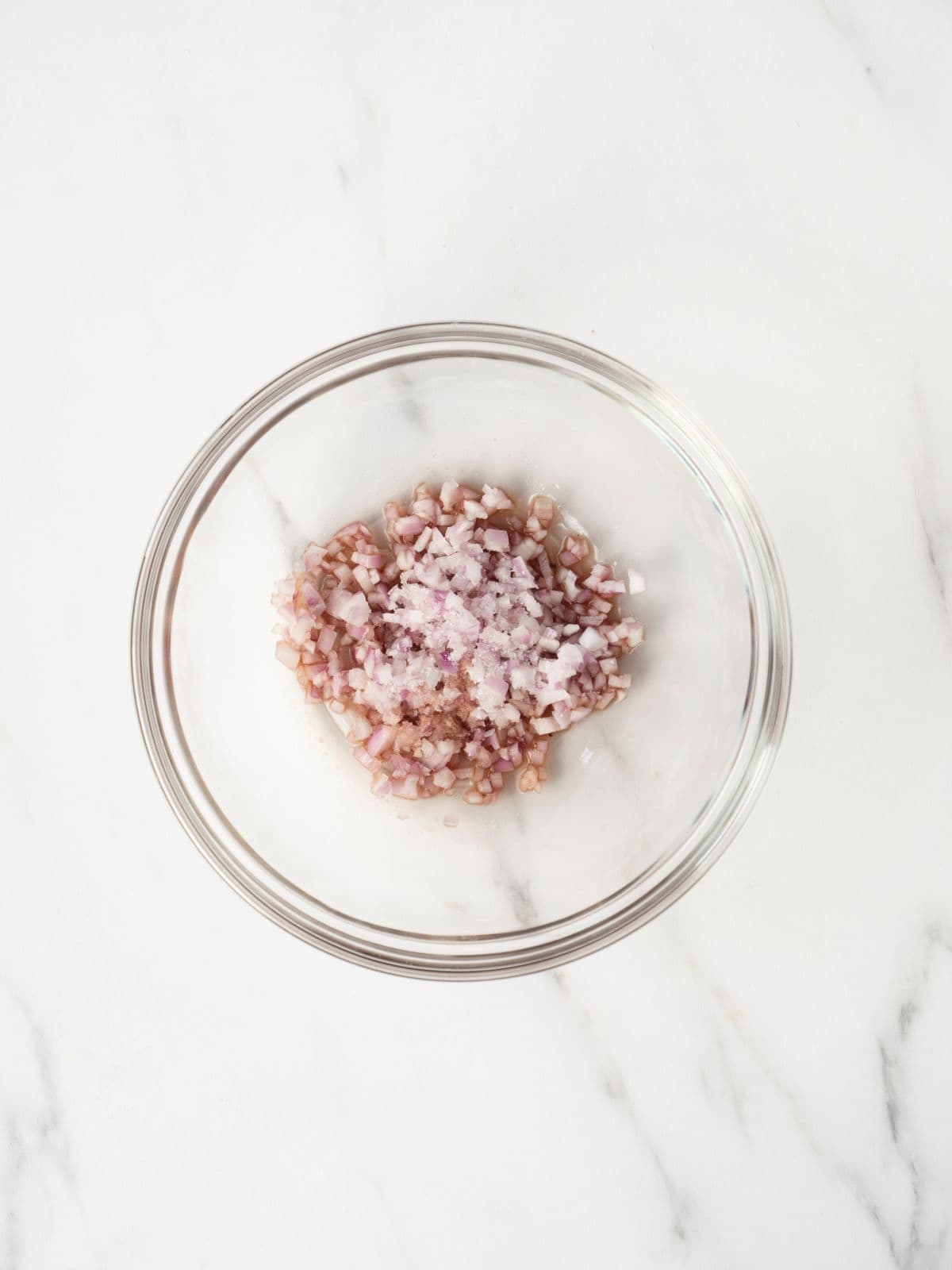 A small glass mixing bowl with finely chopped shallots and vinegar along with salt.