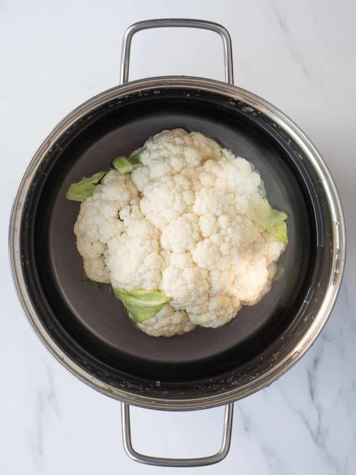 A large pot with a whole cauliflower submerged in water.