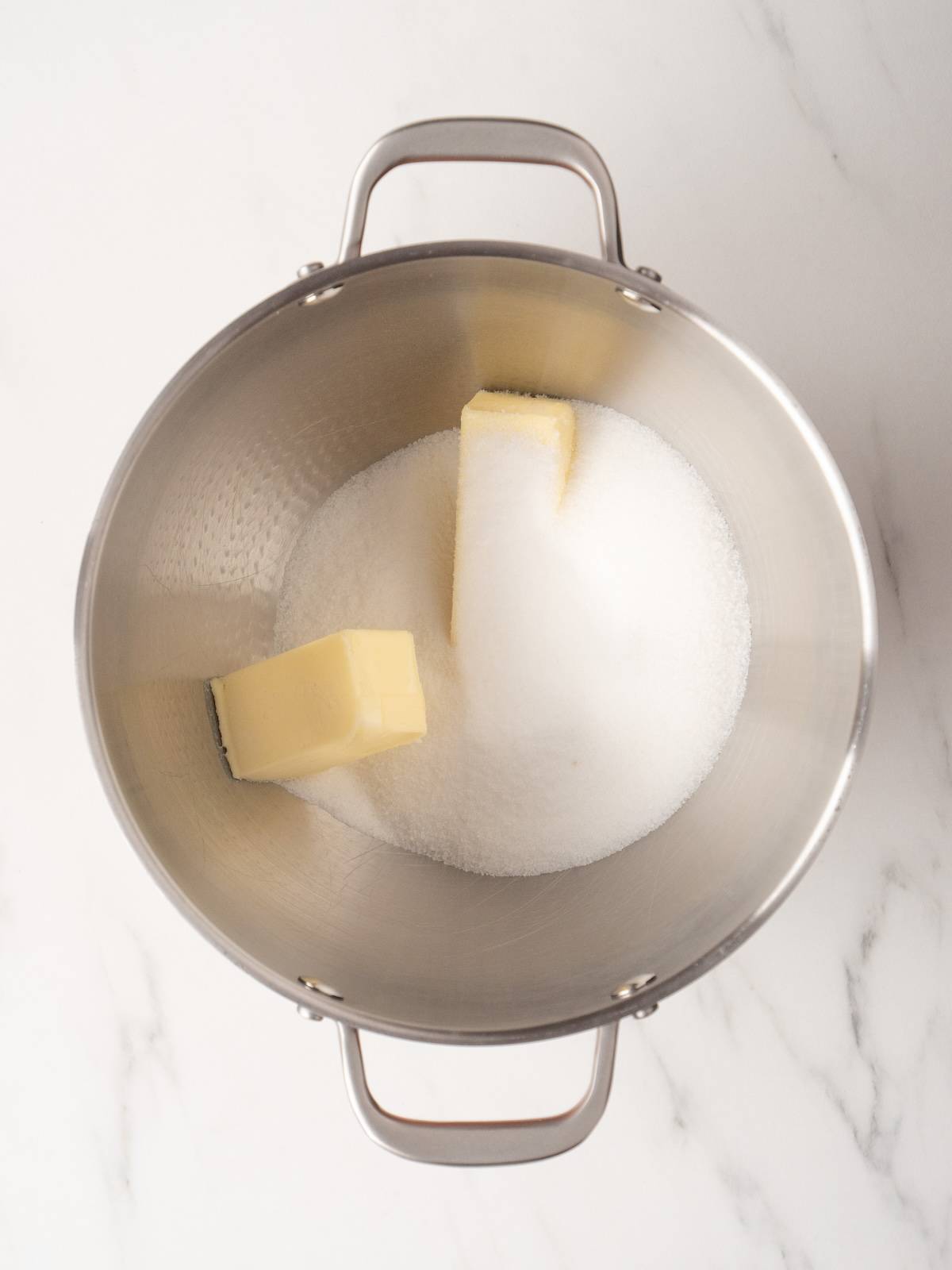 A stand mixer bowl with white sugar and butter added to the bowl.