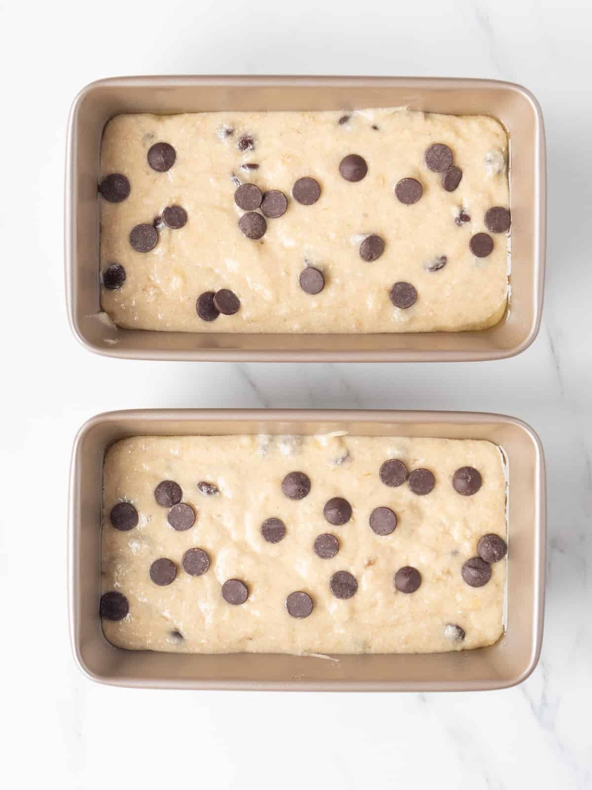 Two 9x5 loaf pans with banana bread batter with chocolate chips on the top, ready to be transferred into the oven.