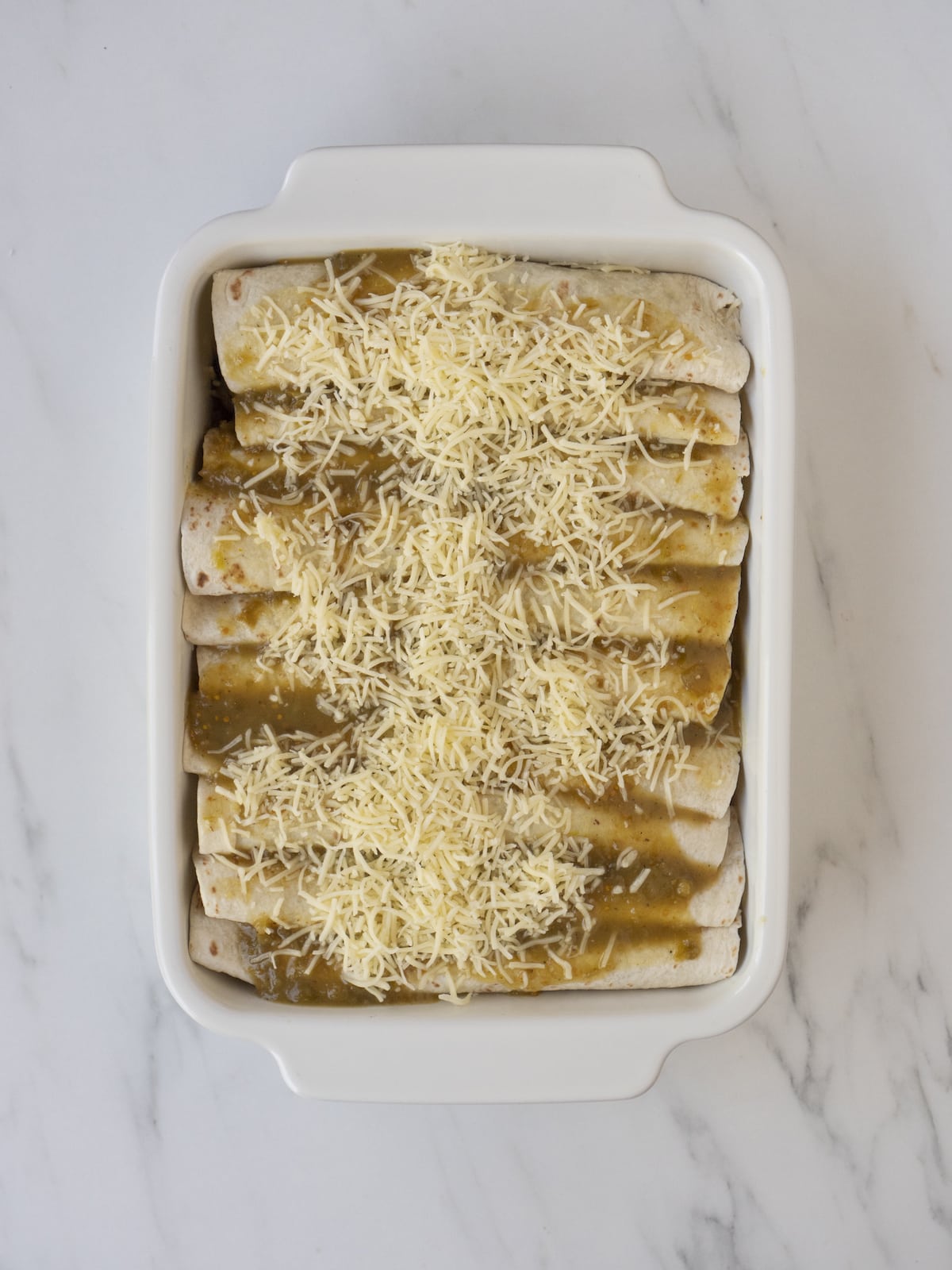 A white rectangular baking dish with vegetarian enchiladas topped with shredded cheese ready to be baked in the oven.