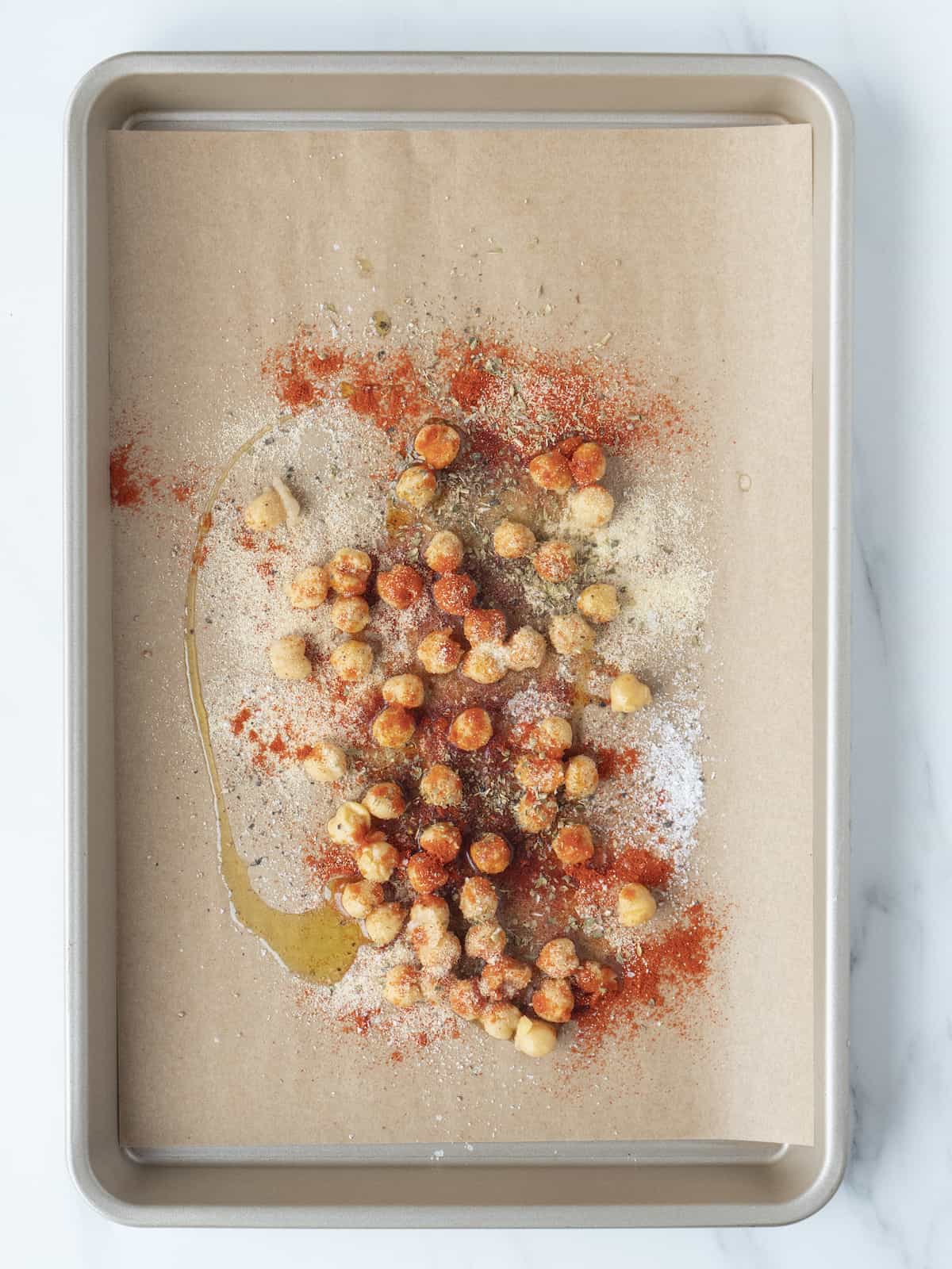 A parchment lined baking sheet with chickpeas tossed in olive oil, salt and spices.