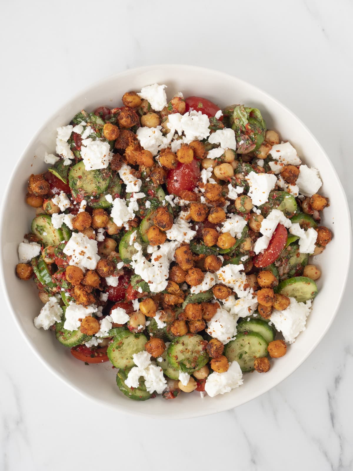 A large white bowl with chopped chickpea salad, topped with feta cheese and crispy chickpeas.
