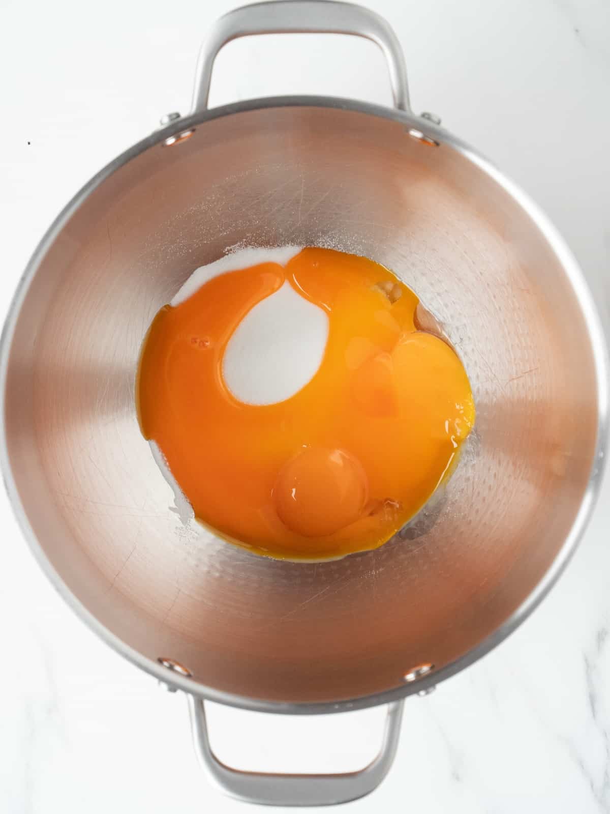 A stand mixer bowl with egg yolk and sugar.