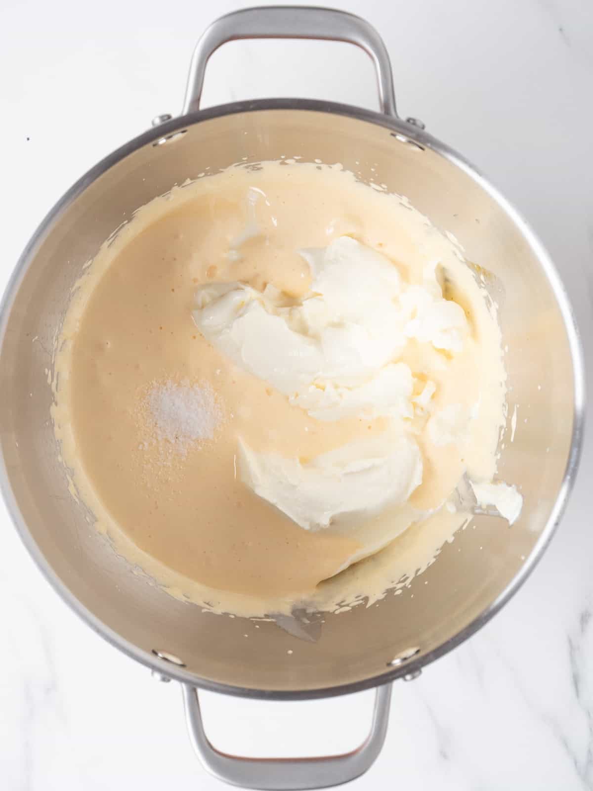 A stand mixer bowl with salt and mascarpone added to the egg yolk and sugar mixture.