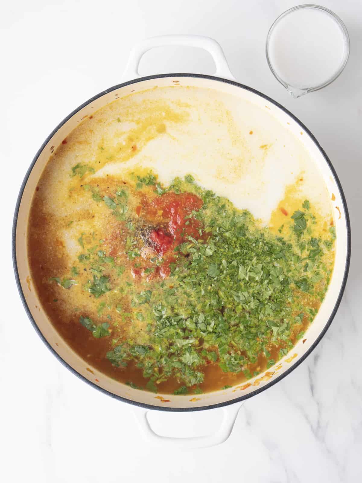 A white dutch oven with lentils and onion base along with coconut milk, water, tomatoes and cilantro.
