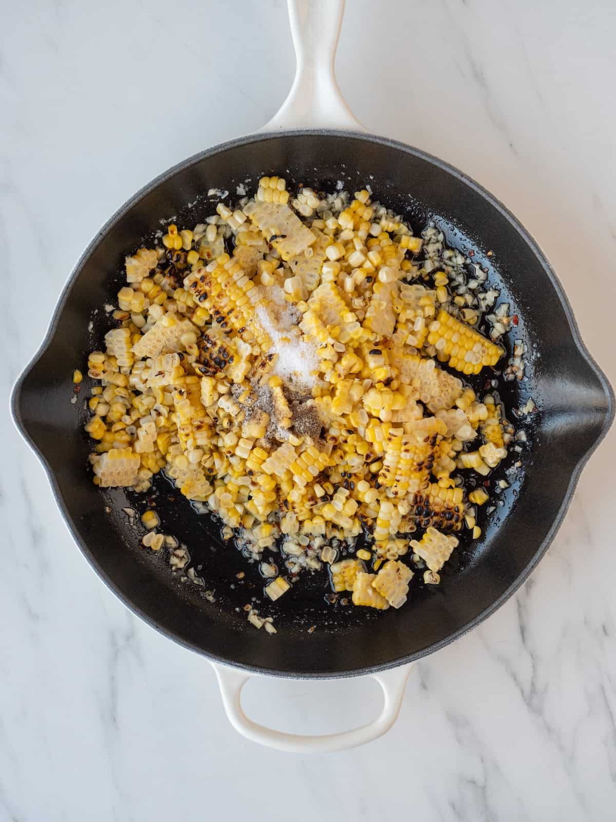 A skillet with the grilled corn kernels removed from the cob.