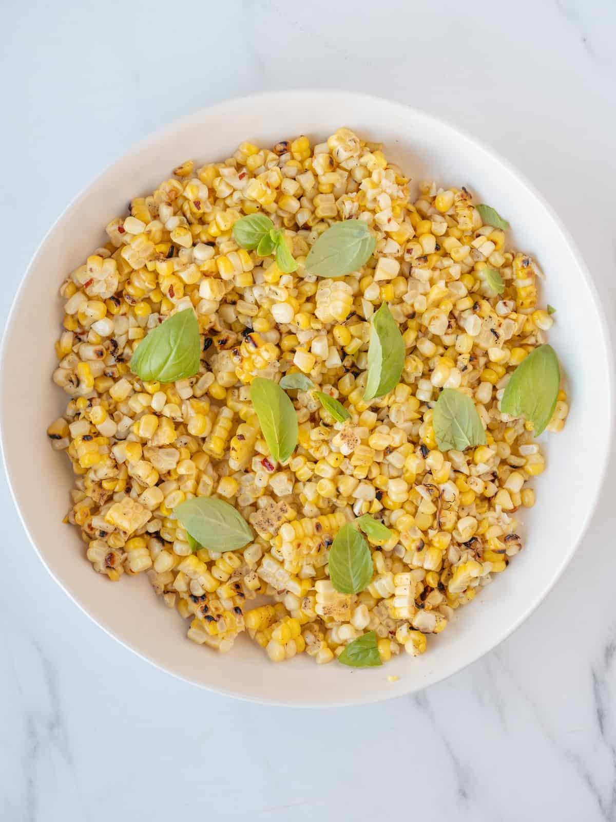 A white bowl with BBQ corn salad garnished with basil leaves.
