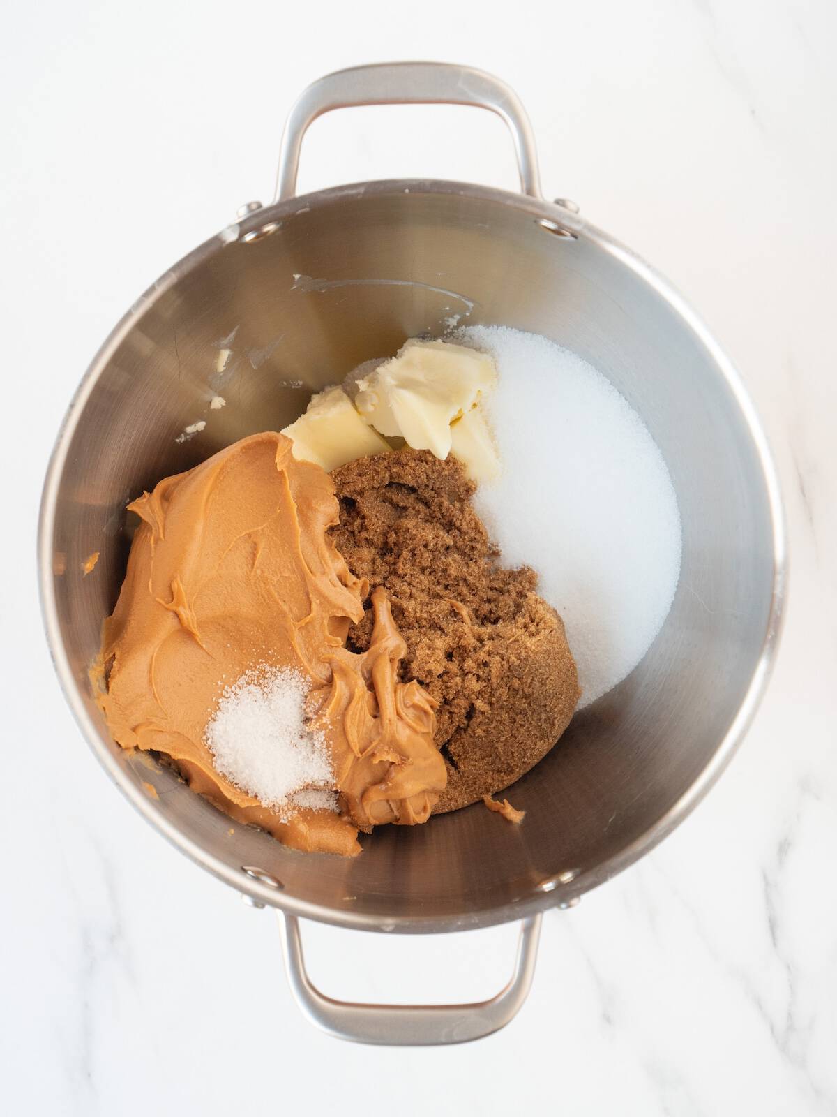 A stand mixer bowl with brown sugar, white sugar, ½ teaspoon salt, peanut butter and butter added to it.