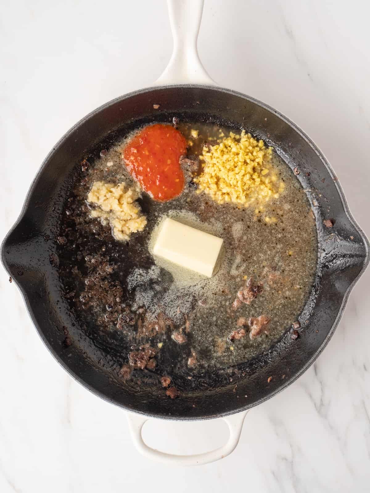 A large skillet with broth, butter, garlic, ginger, and sambal.