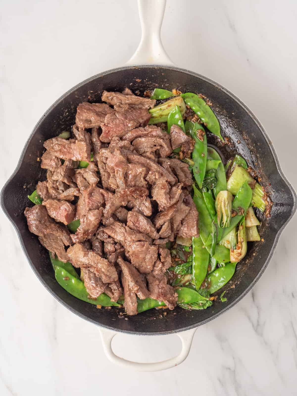 A large skillet with steak stir fry, the steak strips just added on one side and the veggies in the other half.