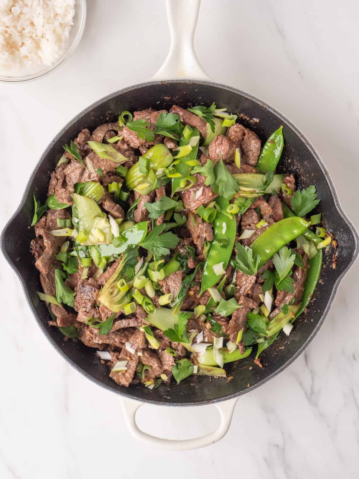 A large skillet with steak stir fry, garnished with parsley and green onion.