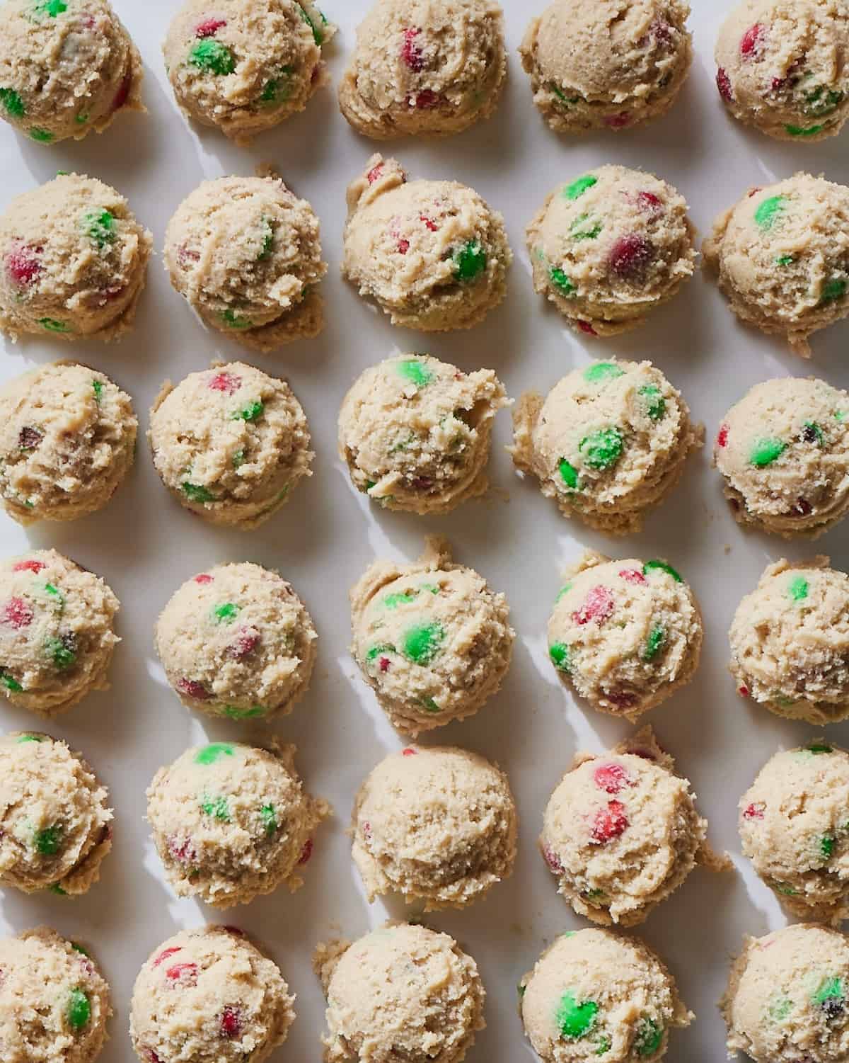 A parchment-lined baking sheet with scoops of Christmas M&M cookie dough.