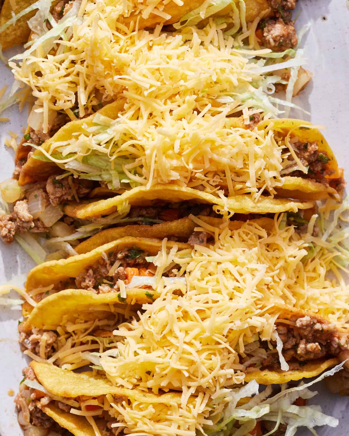 A close-up shot of a white platter with with picadillo hard shell tacos topped with shredded cheese.