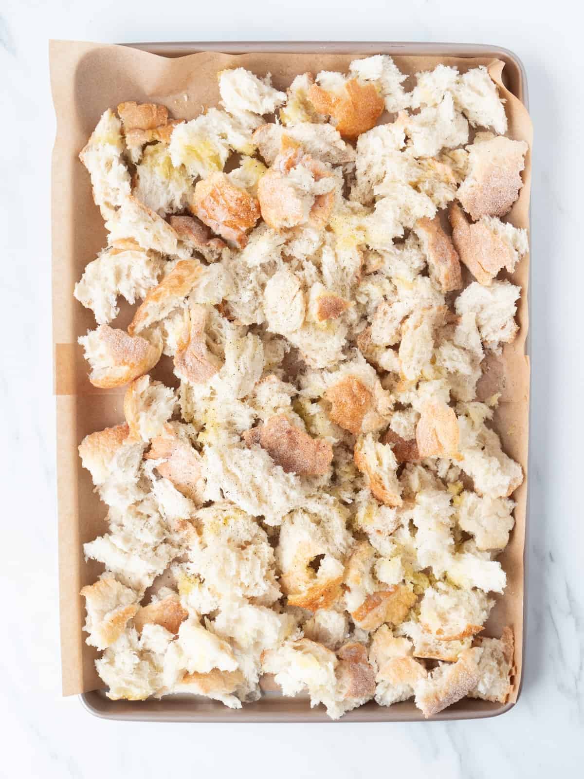 A parchment lined baking sheet with bread torn into pieces, tossed in olive oil and salt and pepper.
