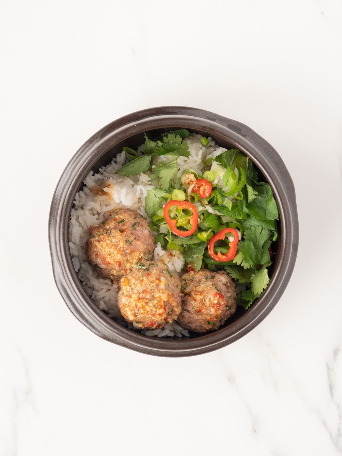 A bowl with rice, herb salad and pork meatballs with sliced fresno chilis.