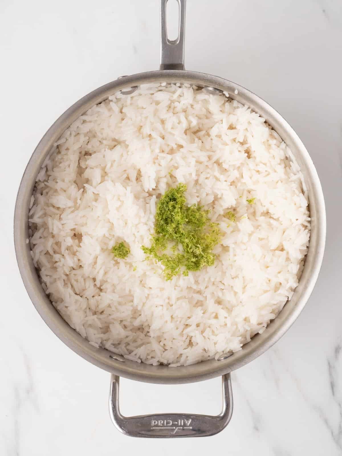 A saucepan with cooked jasmine rice, fluffed and topped with lemon zest.