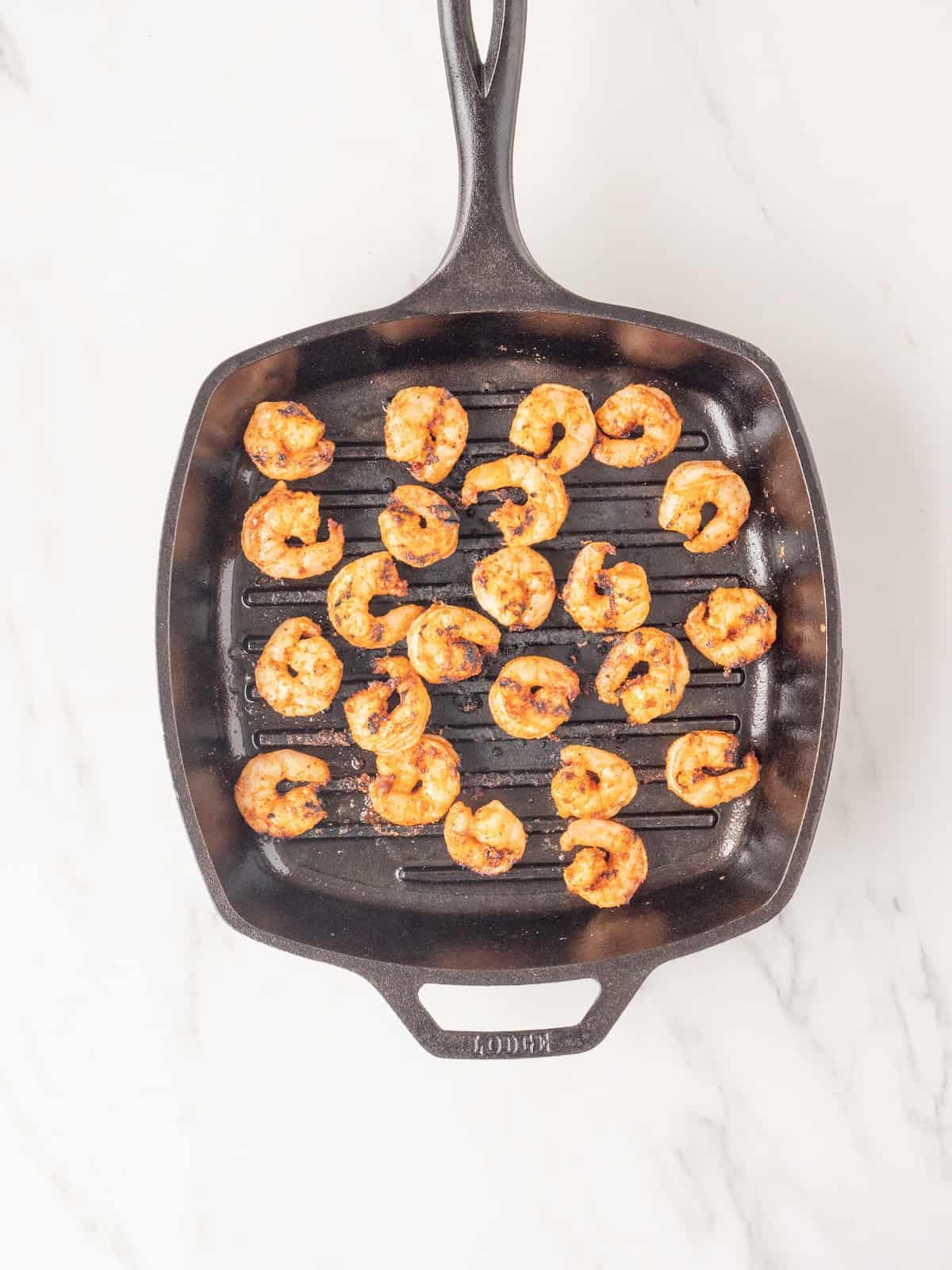 A square grill pan with shrimp being grilled on it.